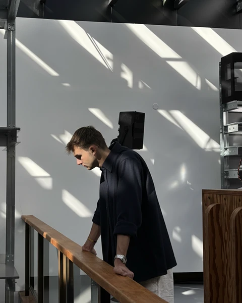 Quentin Freycenon, leaning on a railing in a workshop crossed by the sun.